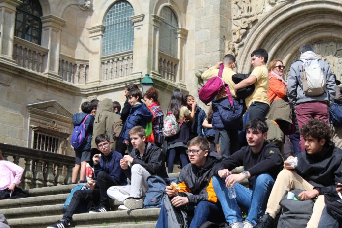 Un grupo de turistas mozos sentados fronte a unha das entradas da Catedral - Xornal de Compostela
